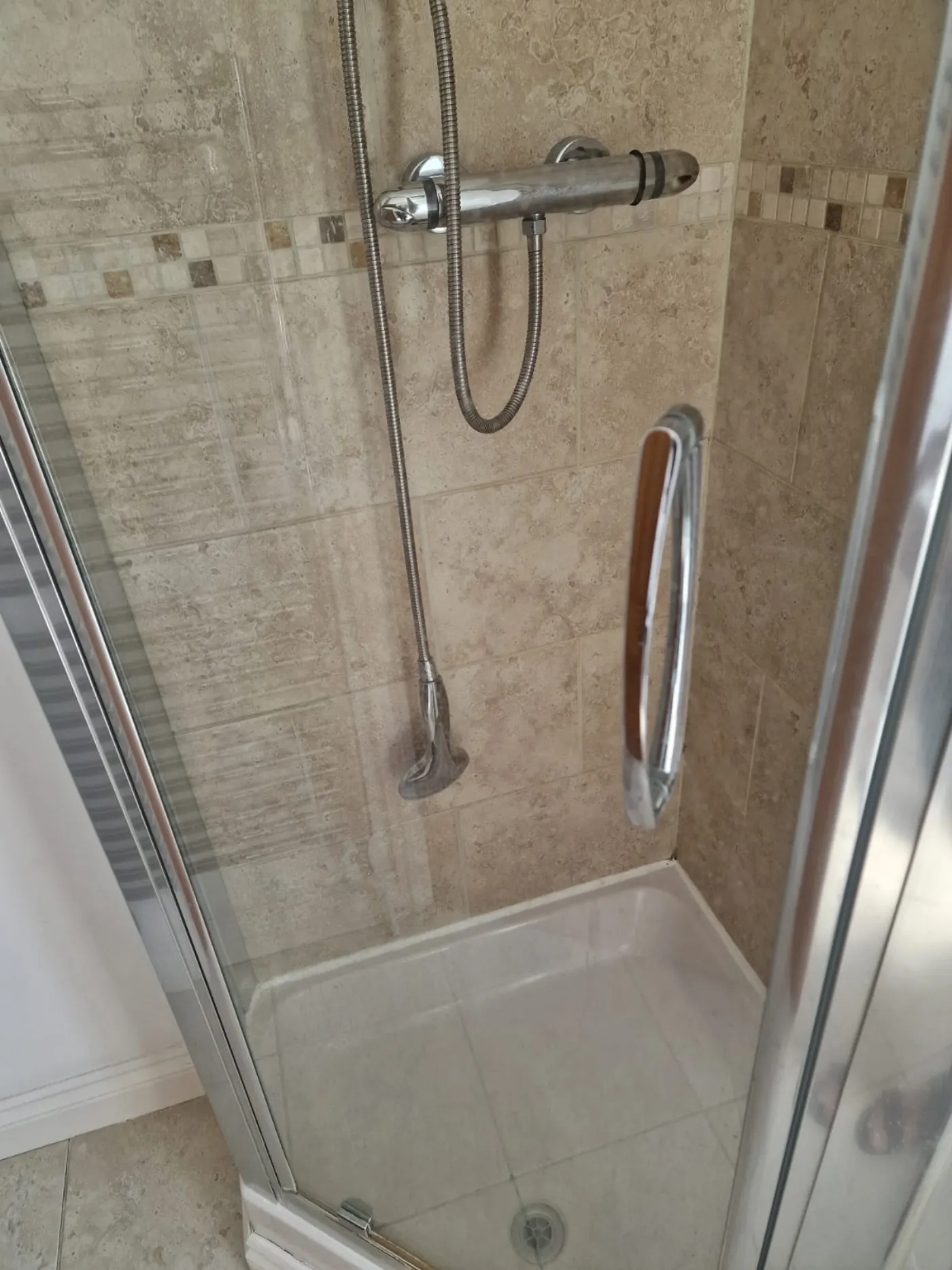 Travertine shower enclosure with limescale on screen and tray before deep clean